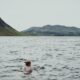 a woman swimming in a lake with mountains in the background